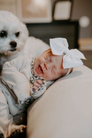 Sleeping newborn wearing a white bow headband photographed in soft natural light.