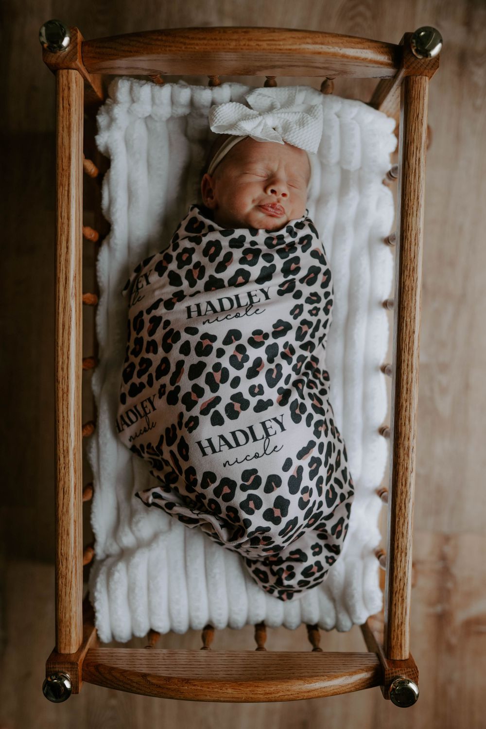 Overhead shot of a newborn baby sleeping in a wooden crib with leopard print blanket.