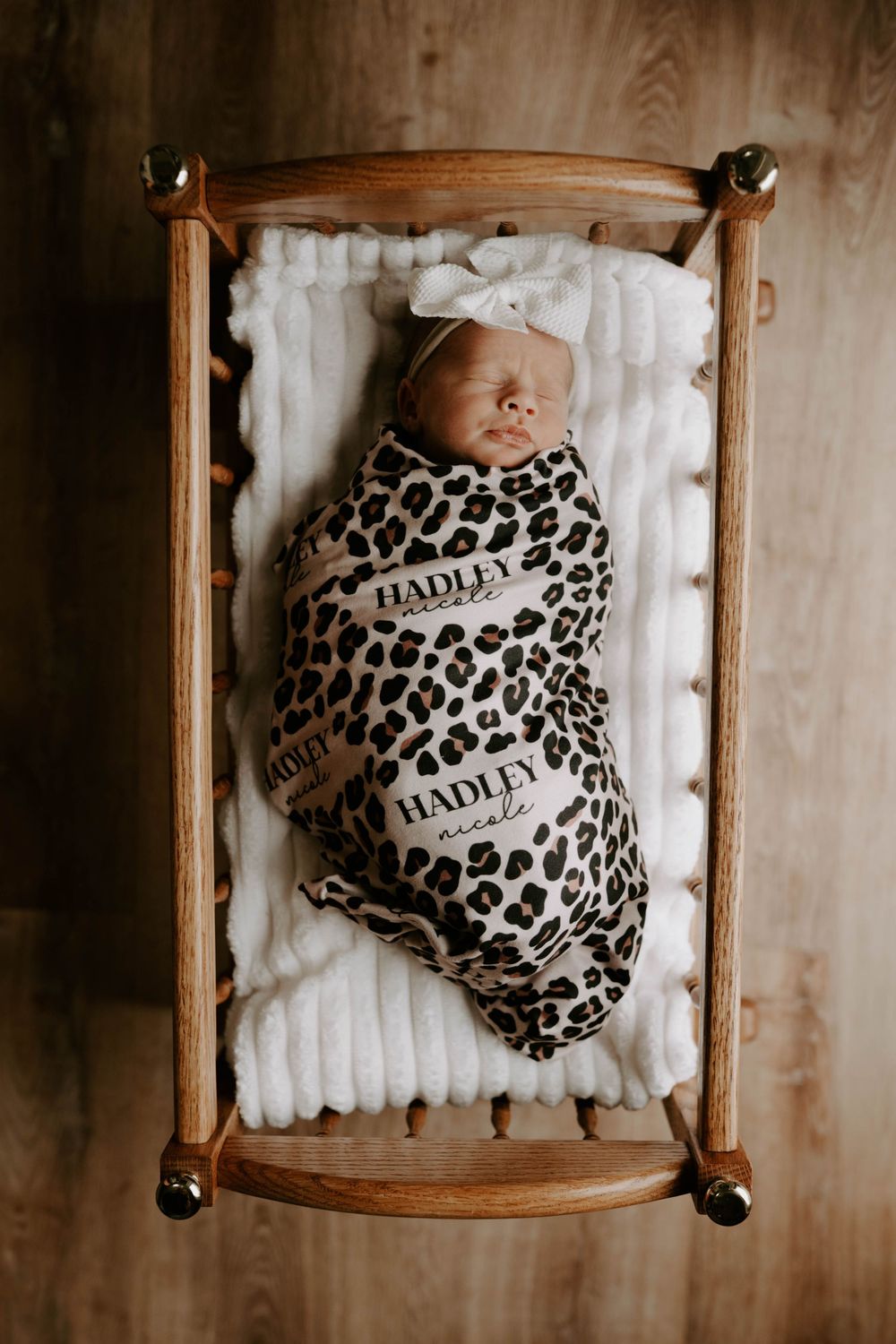 Overhead view of sleeping newborn in leopard print swaddle on wooden bed frame.