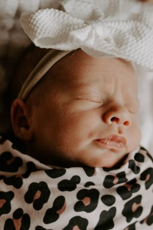 Close-up view of a sleeping newborn wearing a white bow and leopard print swaddle.