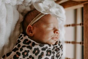 Side profile of a sleeping newborn in a leopard print swaddle and white bow.