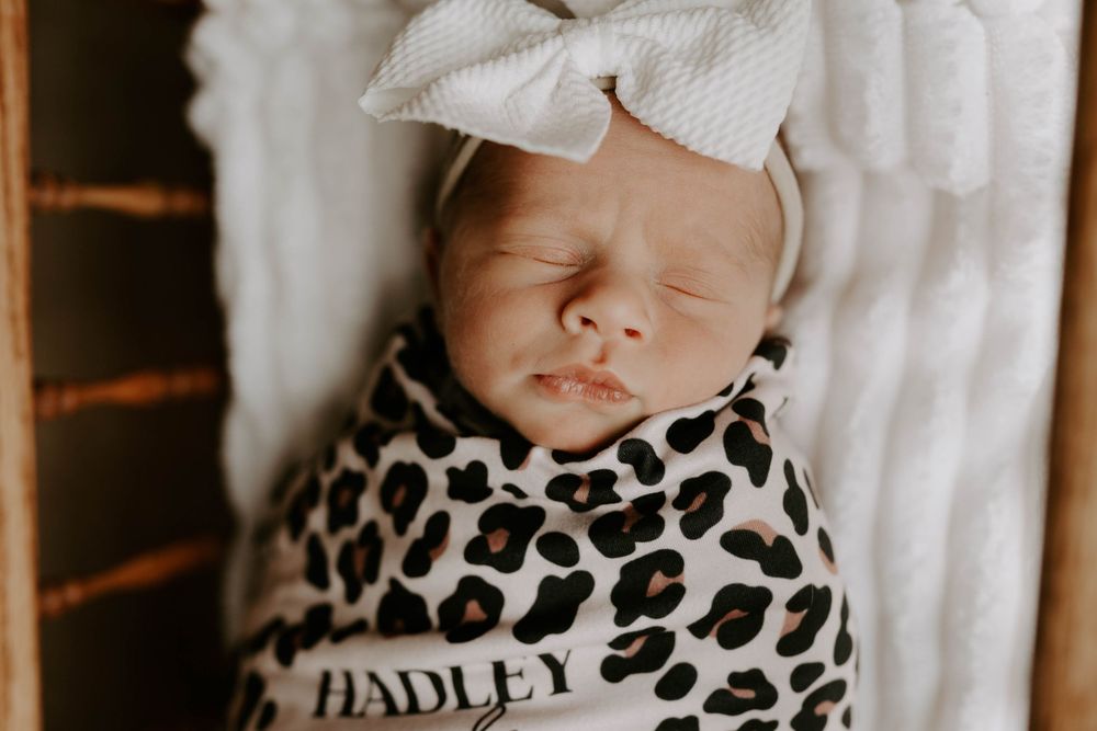 Sleeping newborn in leopard print swaddle and white bow headband.