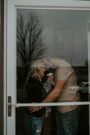 Window reflection of tender family moment with newborn in leopard print.