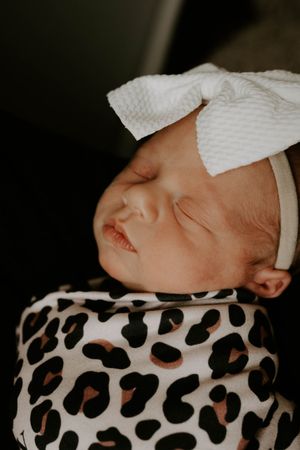 Close up profile of peaceful sleeping baby with white bow and animal print swaddle.