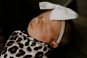 Side view of sleeping infant wrapped in leopard print blanket with white bow.