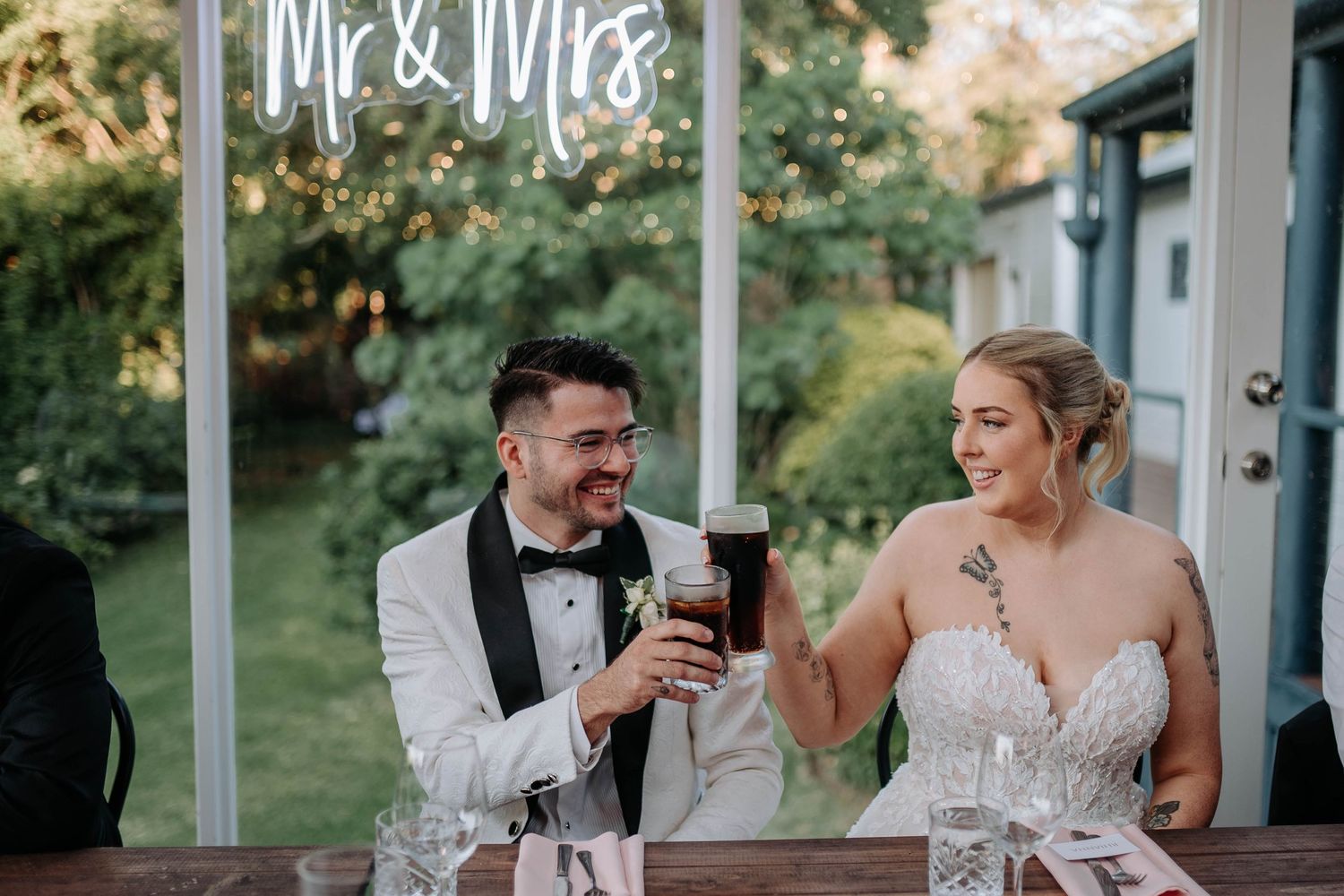 Newlyweds share a laugh while toasting with wine glasses at their outdoor wedding reception.