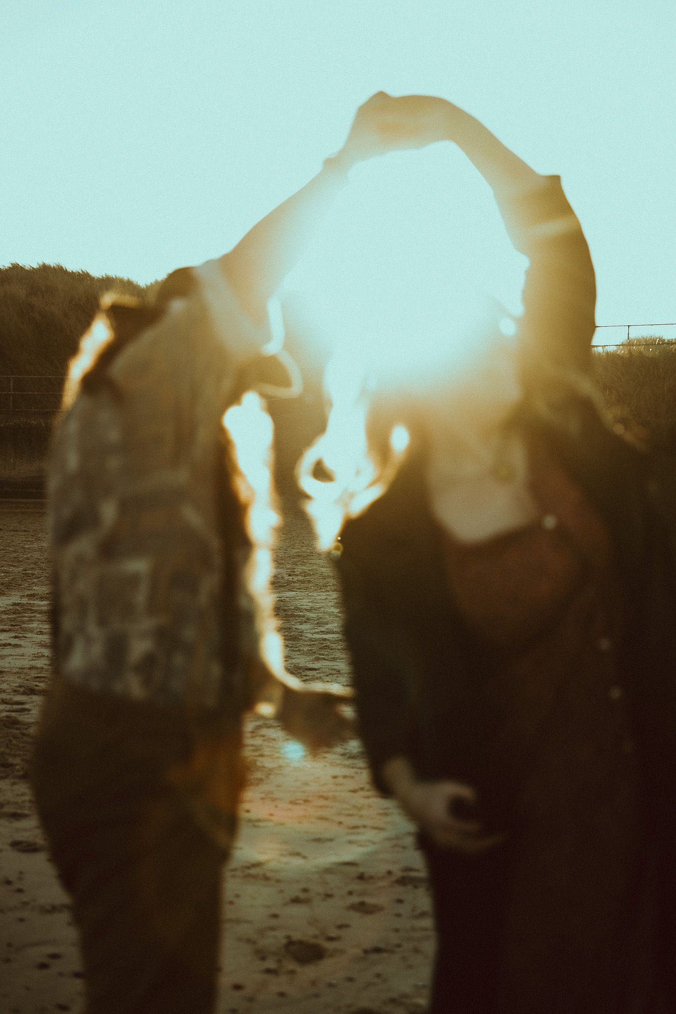 Silhouetted figures forming heart shape with arms against bright sunset.