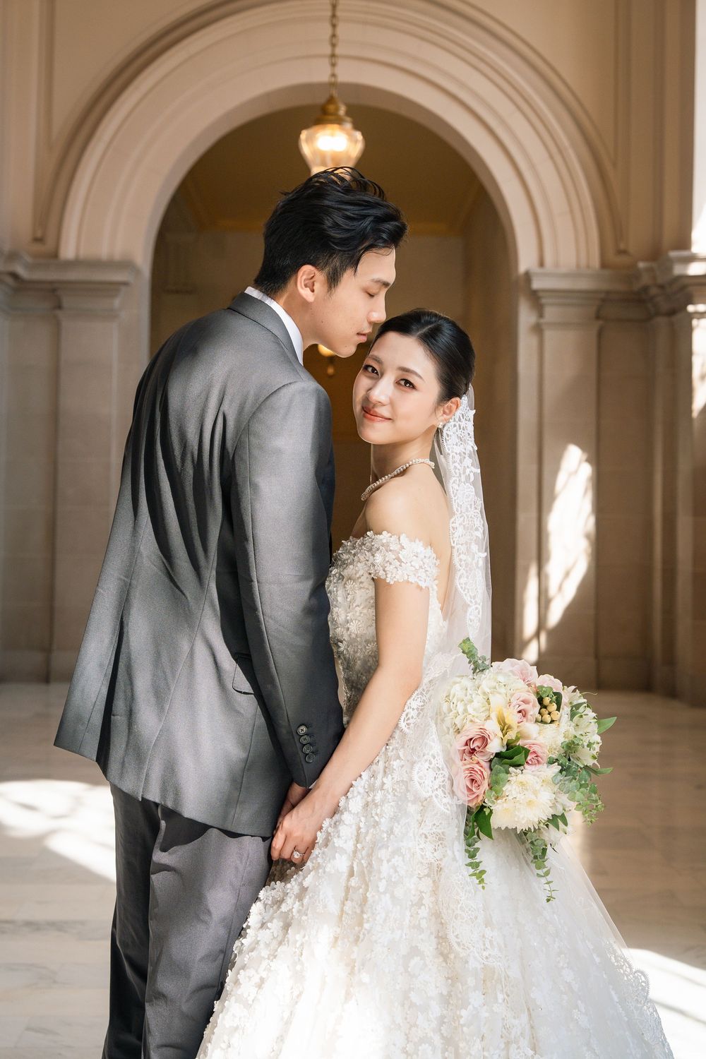 Intimate wedding portraits captured in sunlit classical corridor with elegant formal attire.