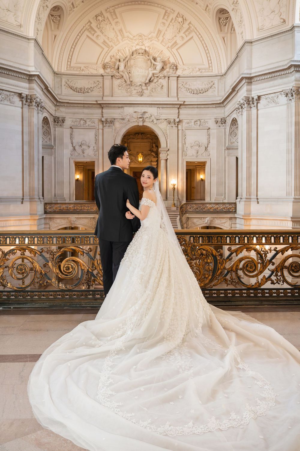 Wedding couple posing in ornate baroque-style hall with dramatic train and gilded details.