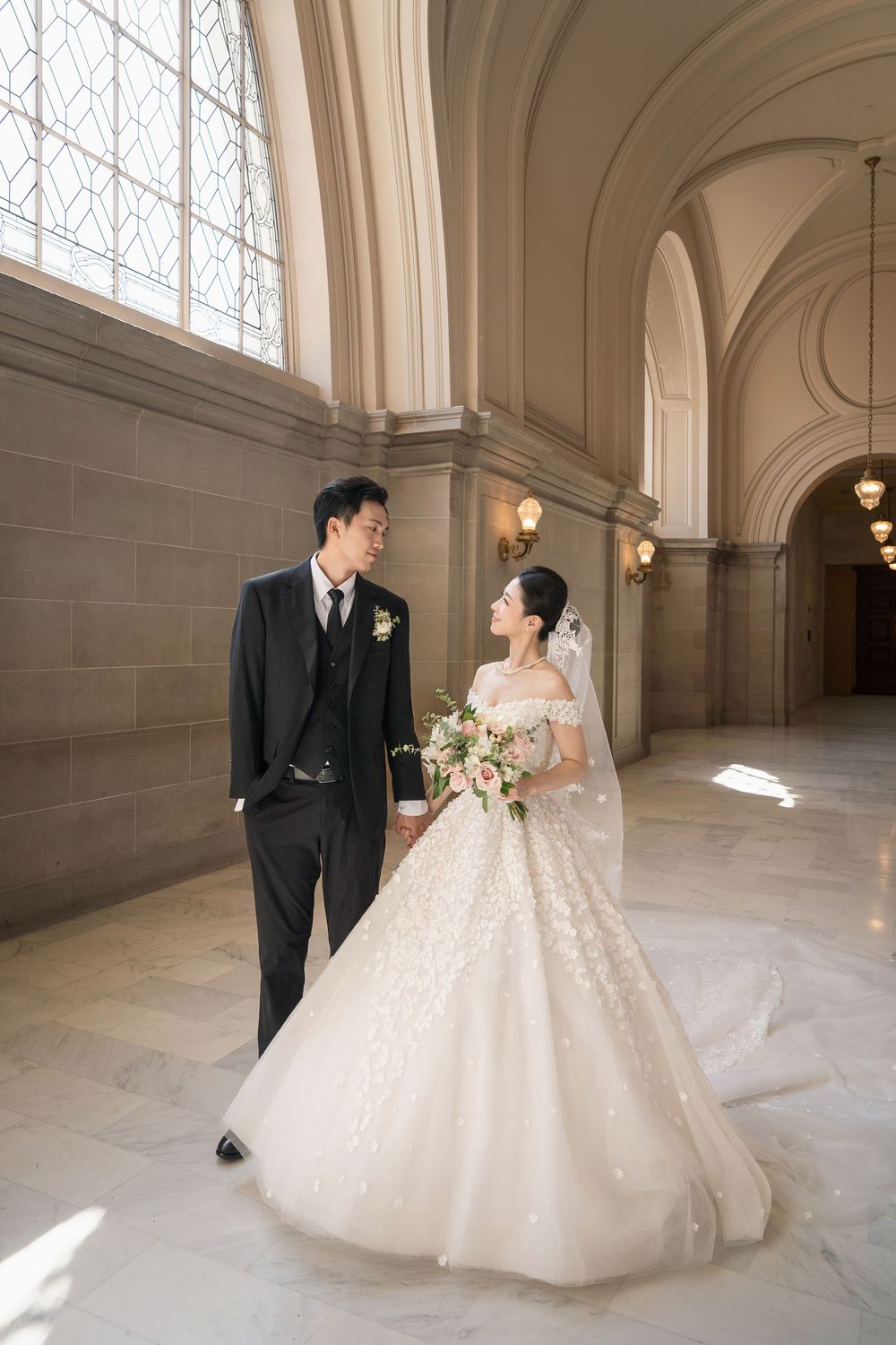 Romantic wedding photoshoot in grand hallway with ornate architecture and natural lighting.