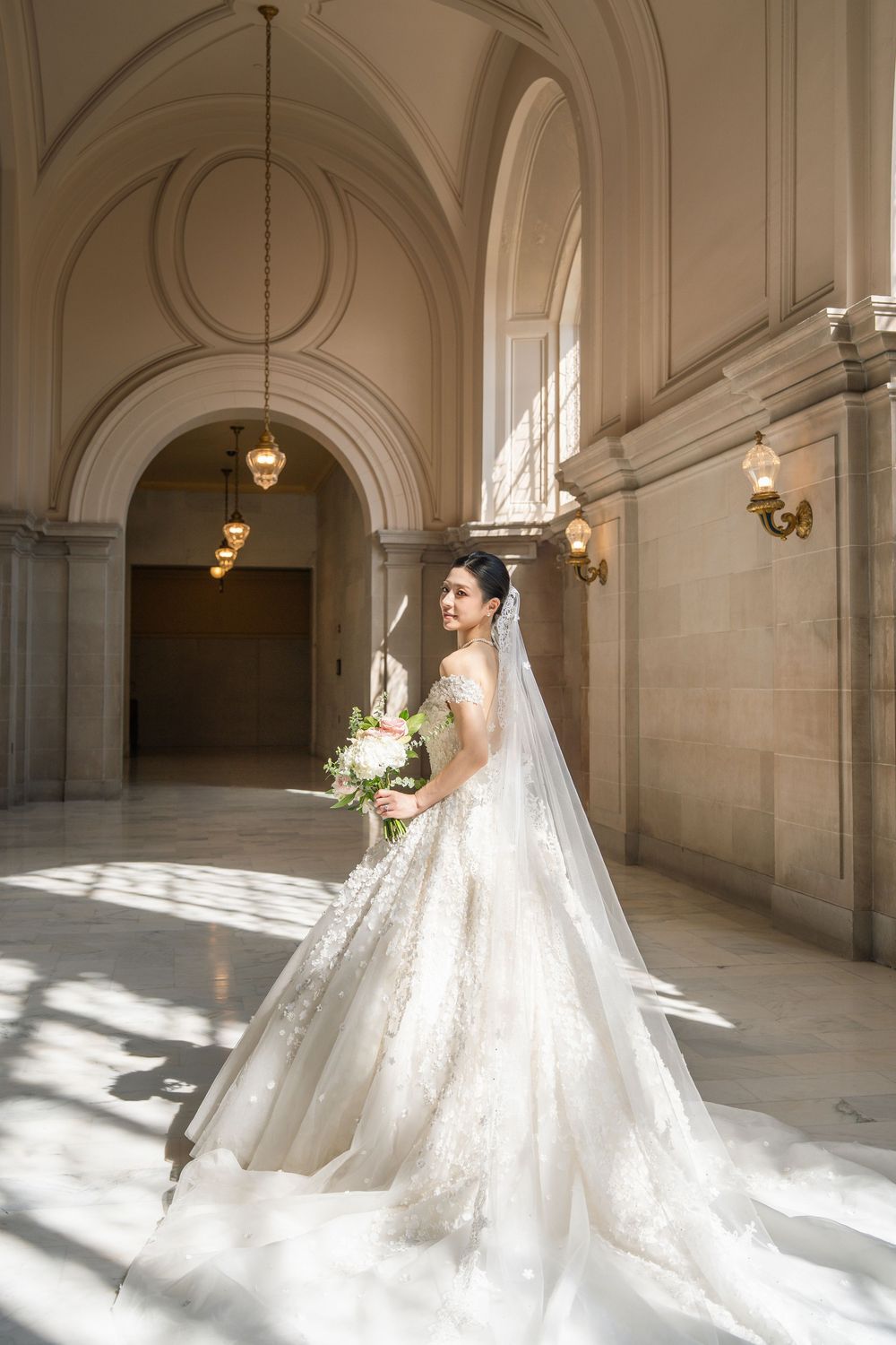 Elegant bridal portrait series showcasing dramatic cathedral veil and luxurious ballgown in sunlit corridor.