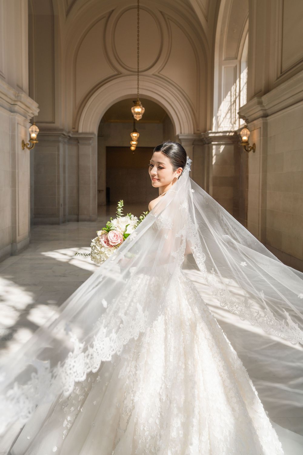 Ethereal bridal photos featuring flowing cathedral veil and detailed lace gown in classic architectural setting.