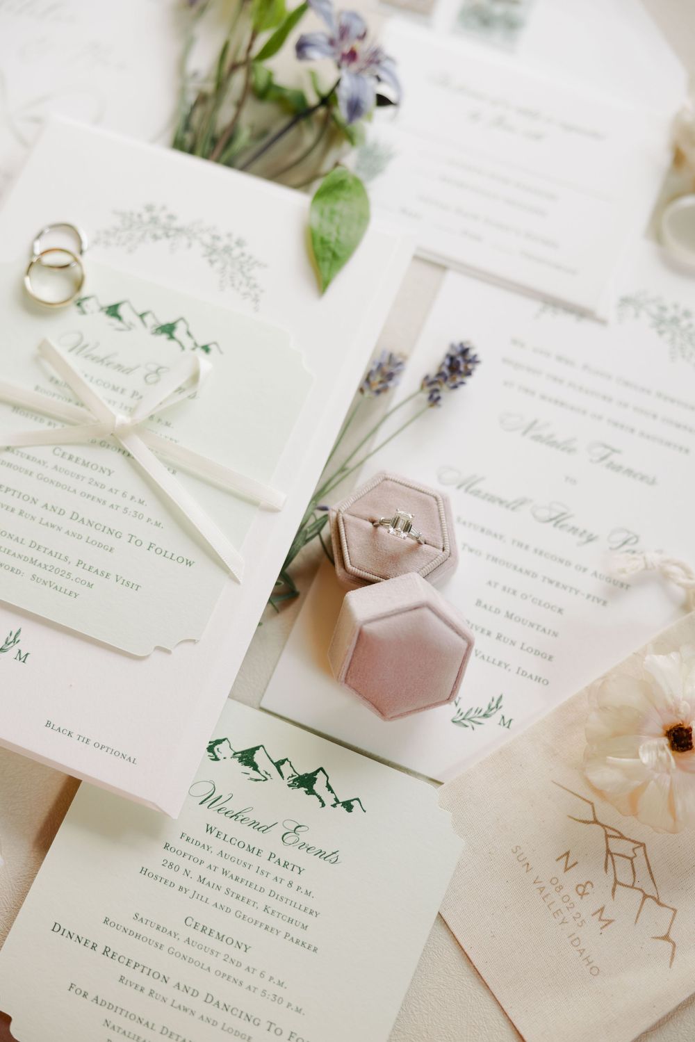 Elegant wedding invitations with delicate floral designs and rings displayed on white paper with greenery accents.