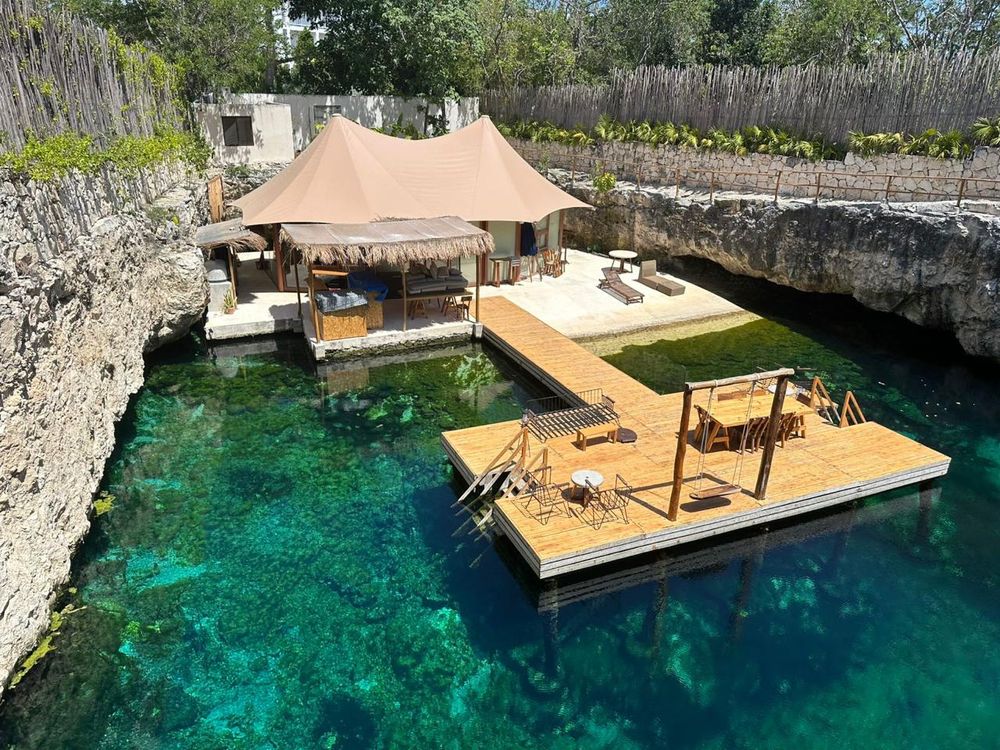 Wooden deck platform extends over crystal clear turquoise waters in a natural limestone cenote in Mexico.