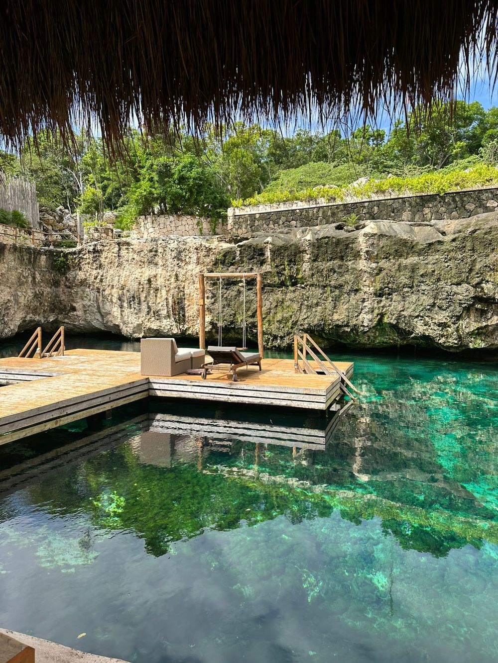 Tropical swimming hole with turquoise water, wooden deck and thatched roof surrounded by limestone cliffs in Mexico.