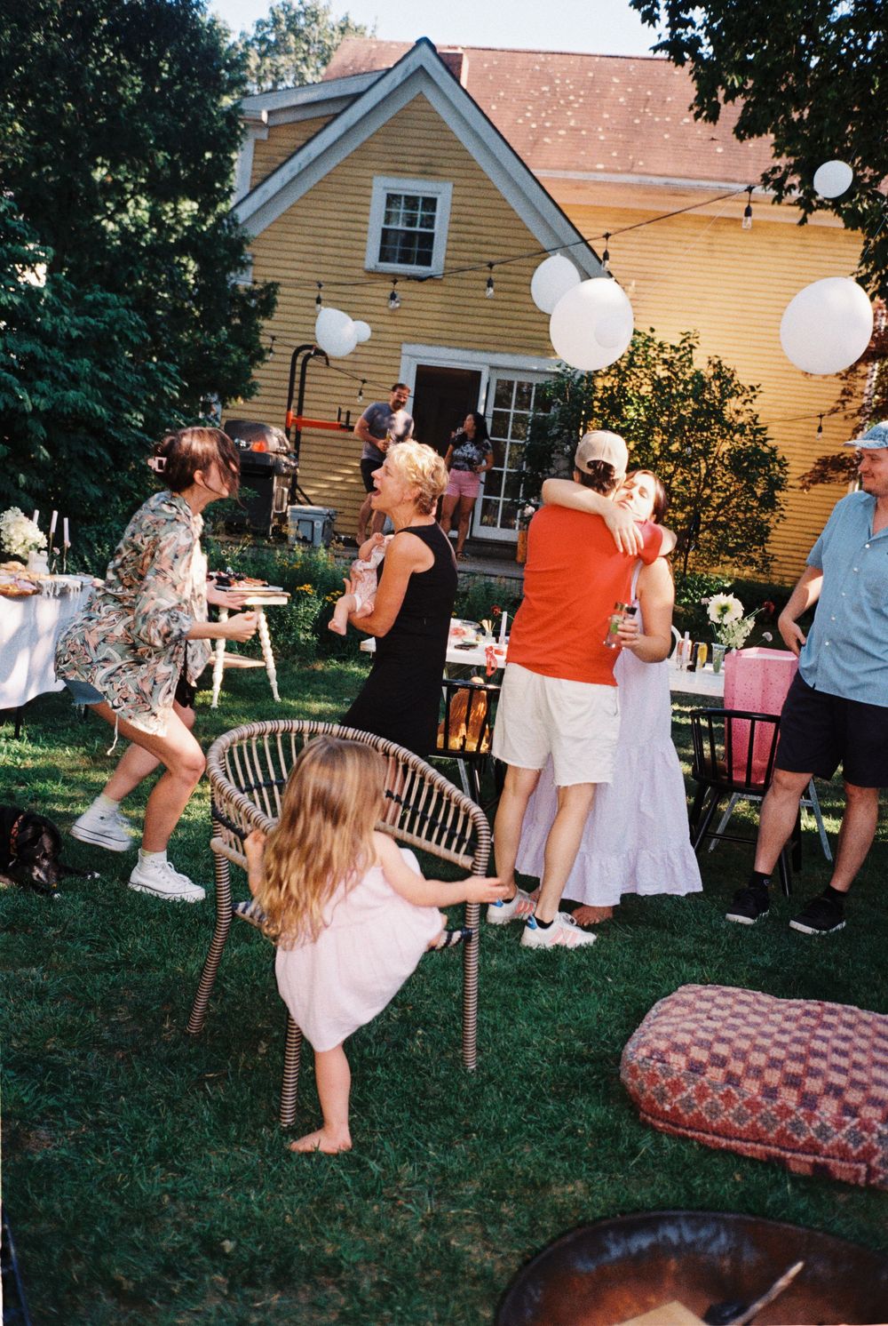 Party scene full of people hugging, a girl climbing a chair a niece and Aunt in lively conversation at a late summer baby shower in Maine.