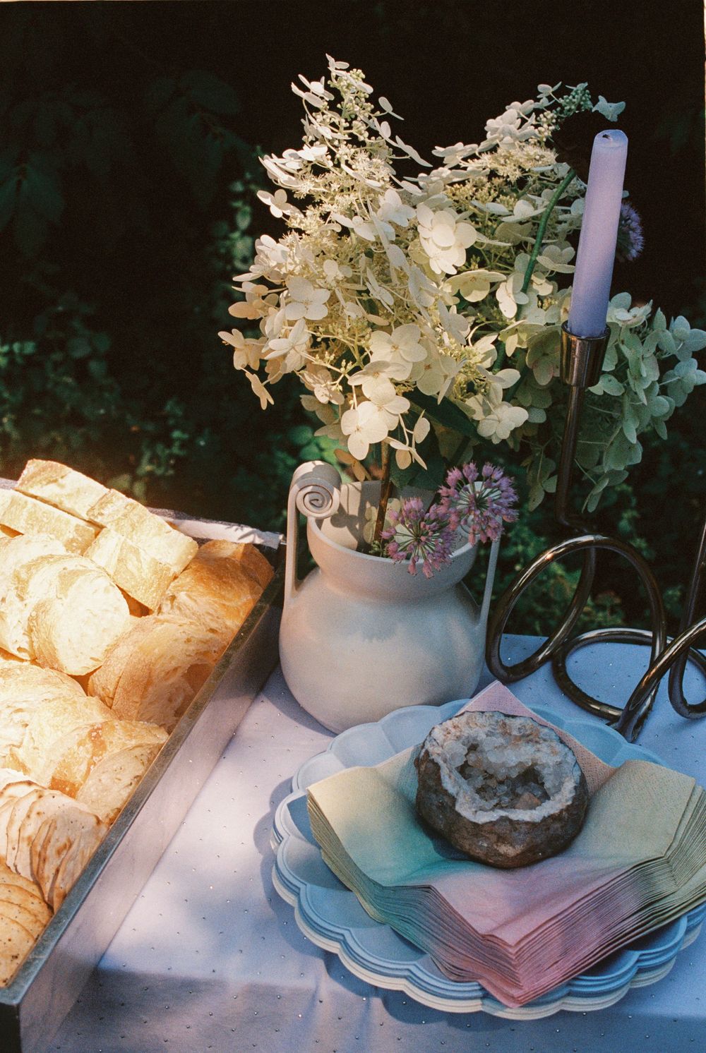 Handmade vase with fresh flowers, fresh cut bread and pastel colored napkins adorn the table at a newborn baby's Sprinkle Shower party.