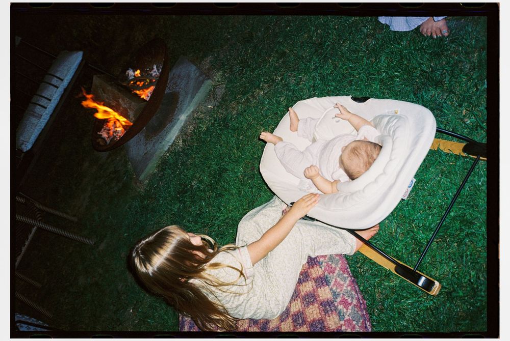 Big sister rocks her new baby sister outside next to the fire late into the night after a sprinkle baby shower in August in South Portland.