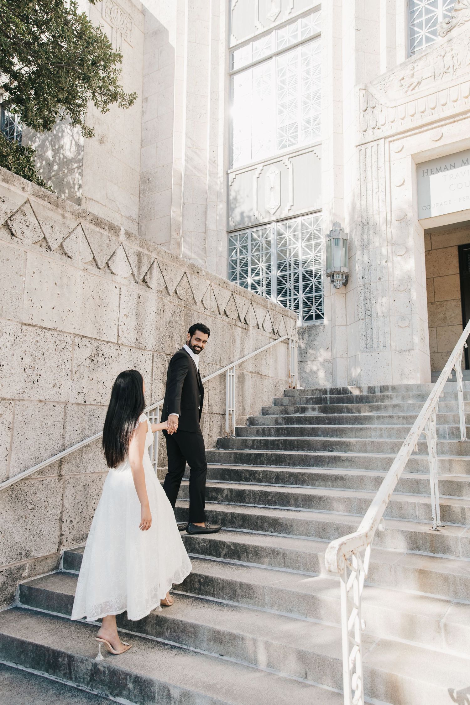 A couple in formal attire shares a romantic moment on elegant stone steps of a historic building.