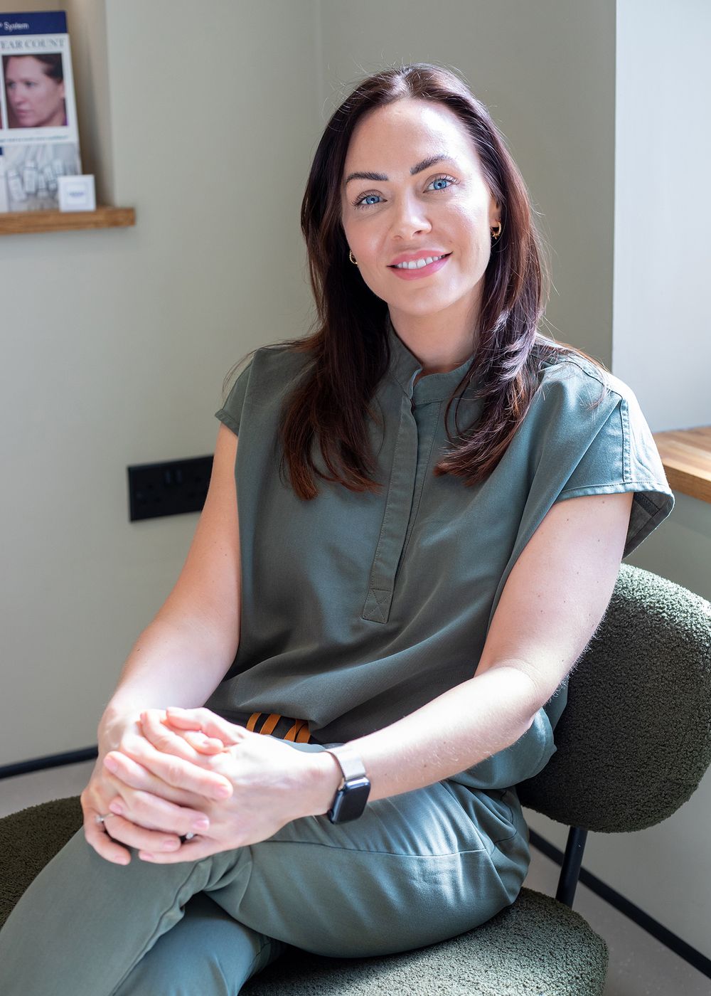 A person in a sage green sleeveless top sits casually on a dark chair in various relaxed poses.