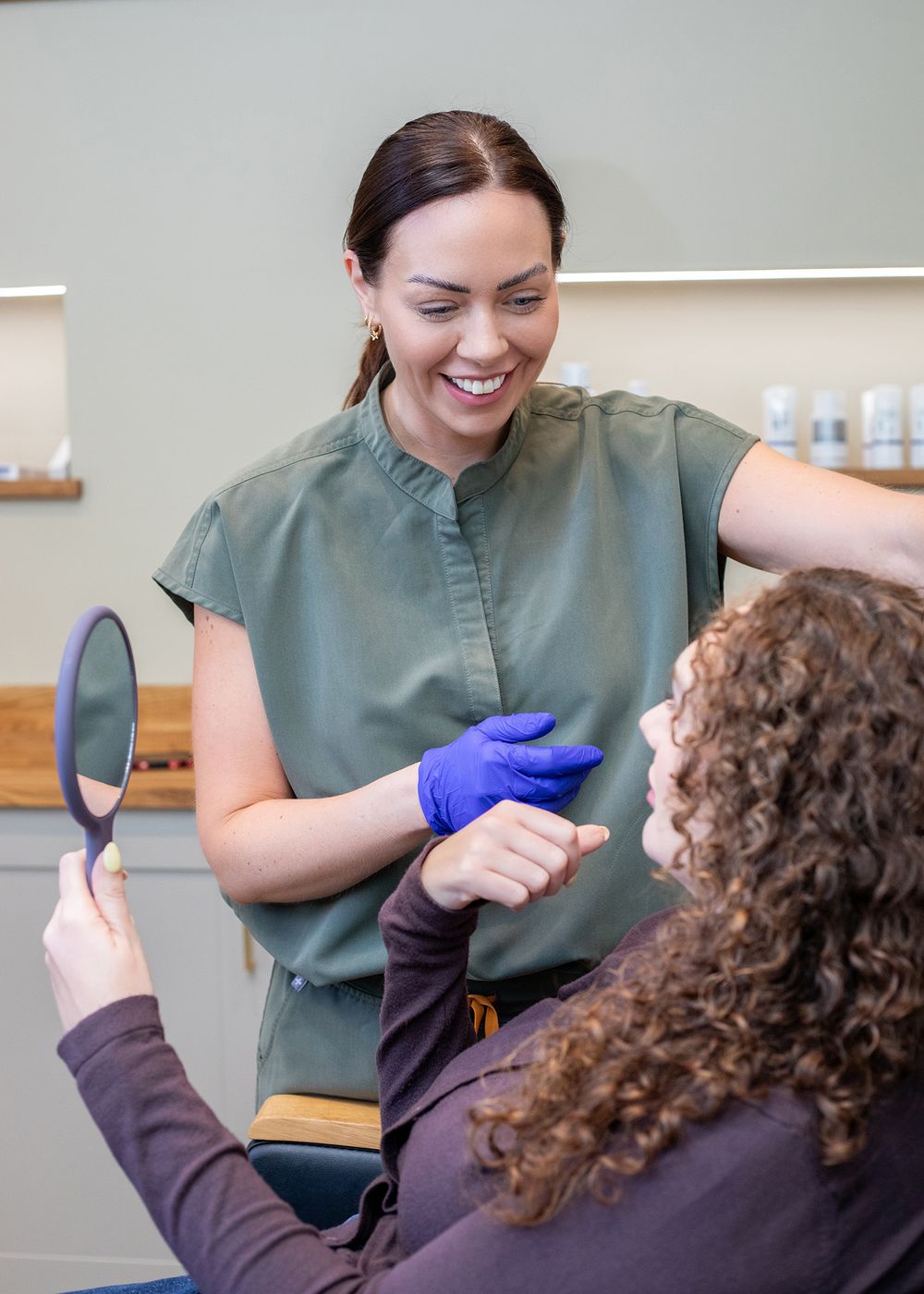 Healthcare professional in green scrubs and purple gloves performs a medical examination on a patient in a clinical setting.