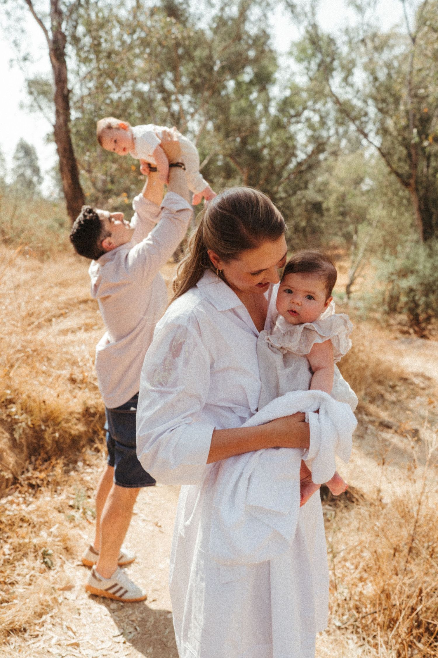 A family in white outfits plays together in a sunny outdoor setting.