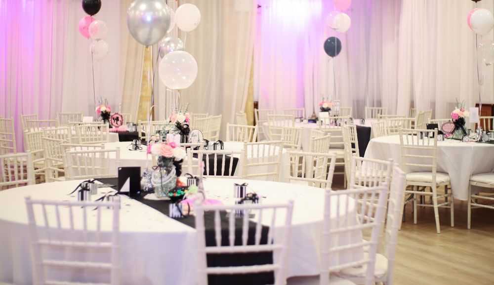 An elegant wedding reception venue with white chairs, draped fabric walls, and crystal chandeliers creating a romantic atmosphere.