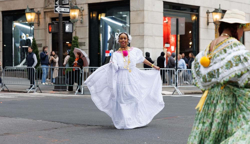 Performers in traditional white and green dresses dance together during a street festival celebration.