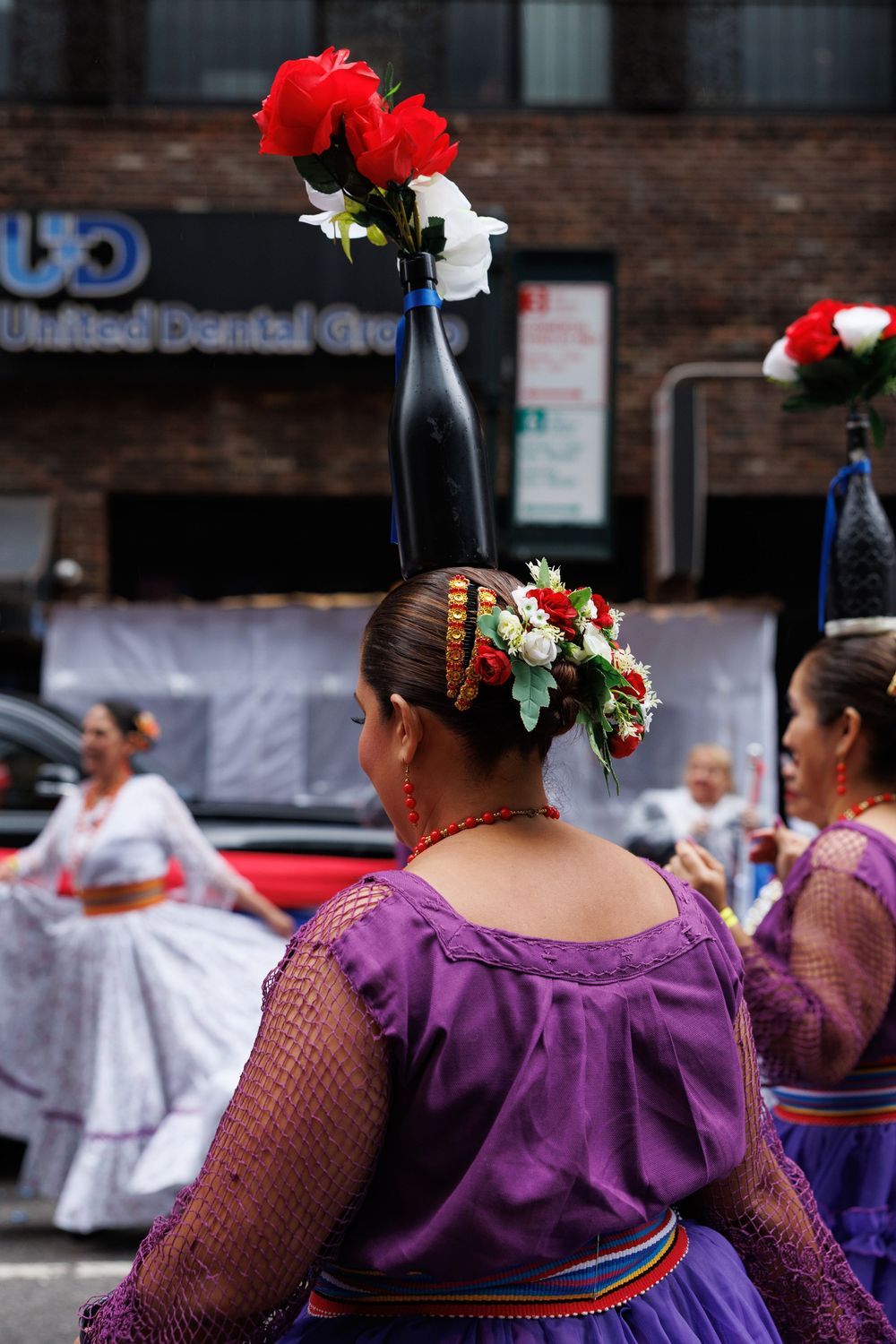 Traditional dancers in purple dresses with red flowers in their hair perform at a cultural festival.