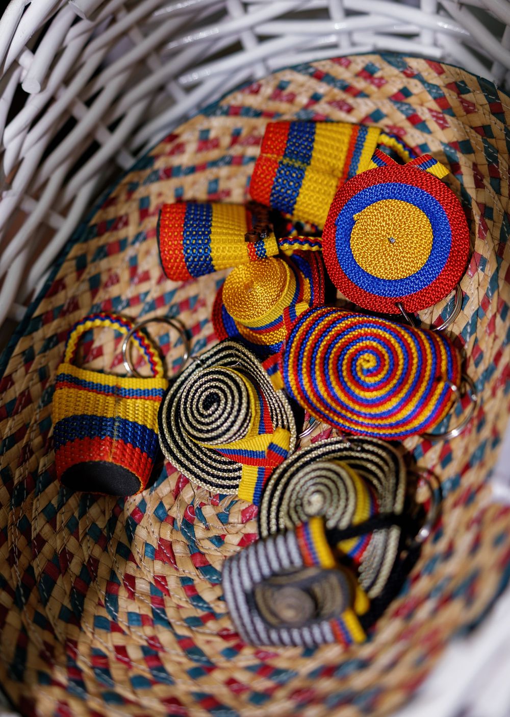Colorful woven bracelets and accessories with spiral patterns in red, yellow, and blue displayed in a wicker basket.