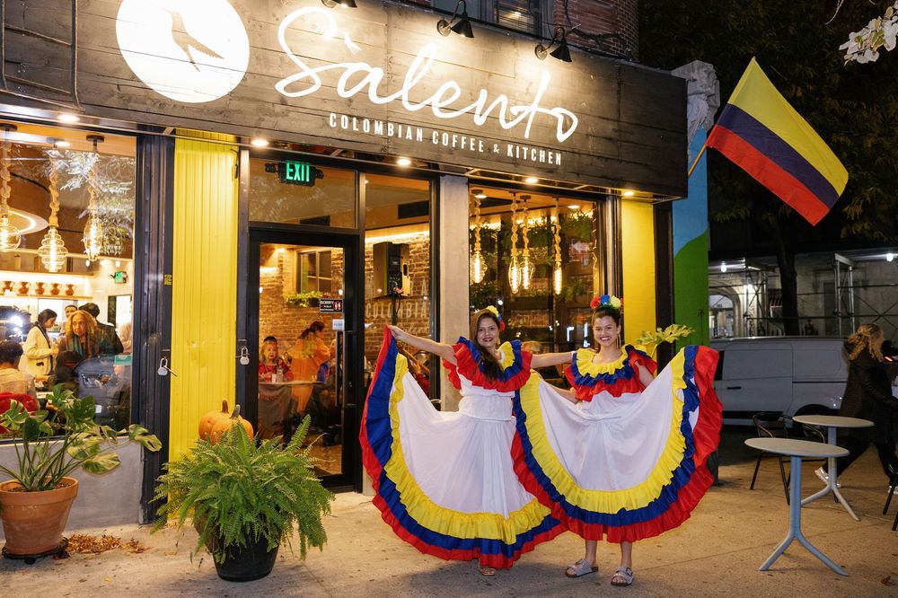 Colombian flags and colorful decorations adorn the entrance of a modern restaurant with warm lighting.