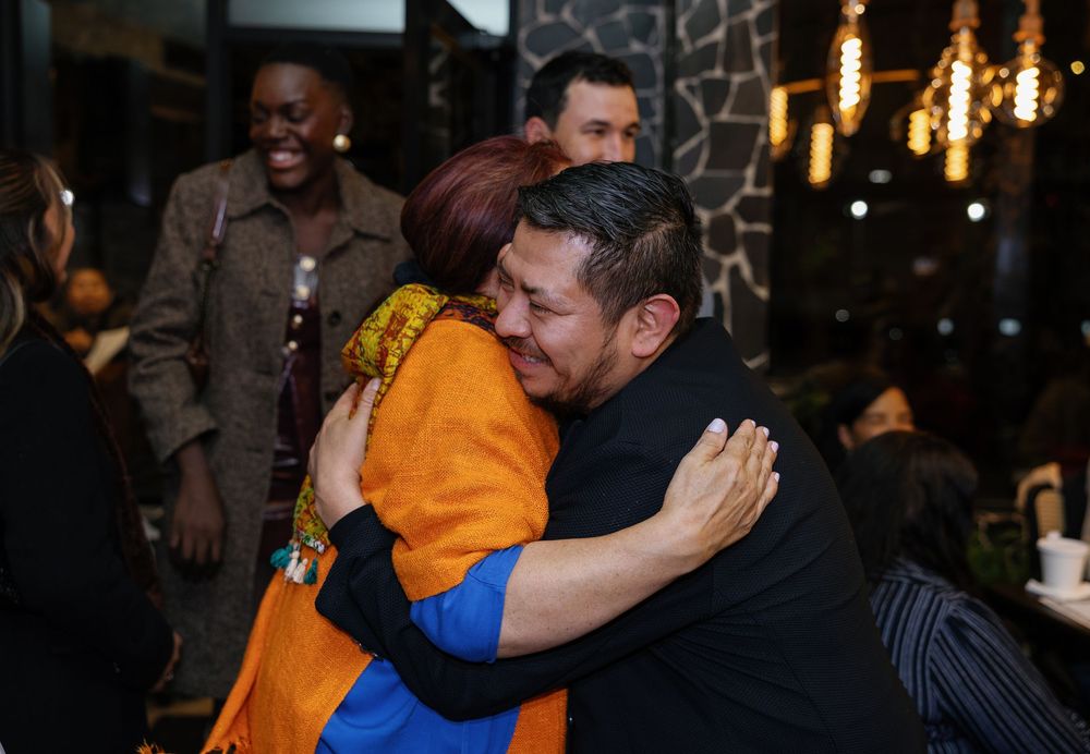 Two people share a warm hug at a social gathering inside a restaurant with ambient lighting.