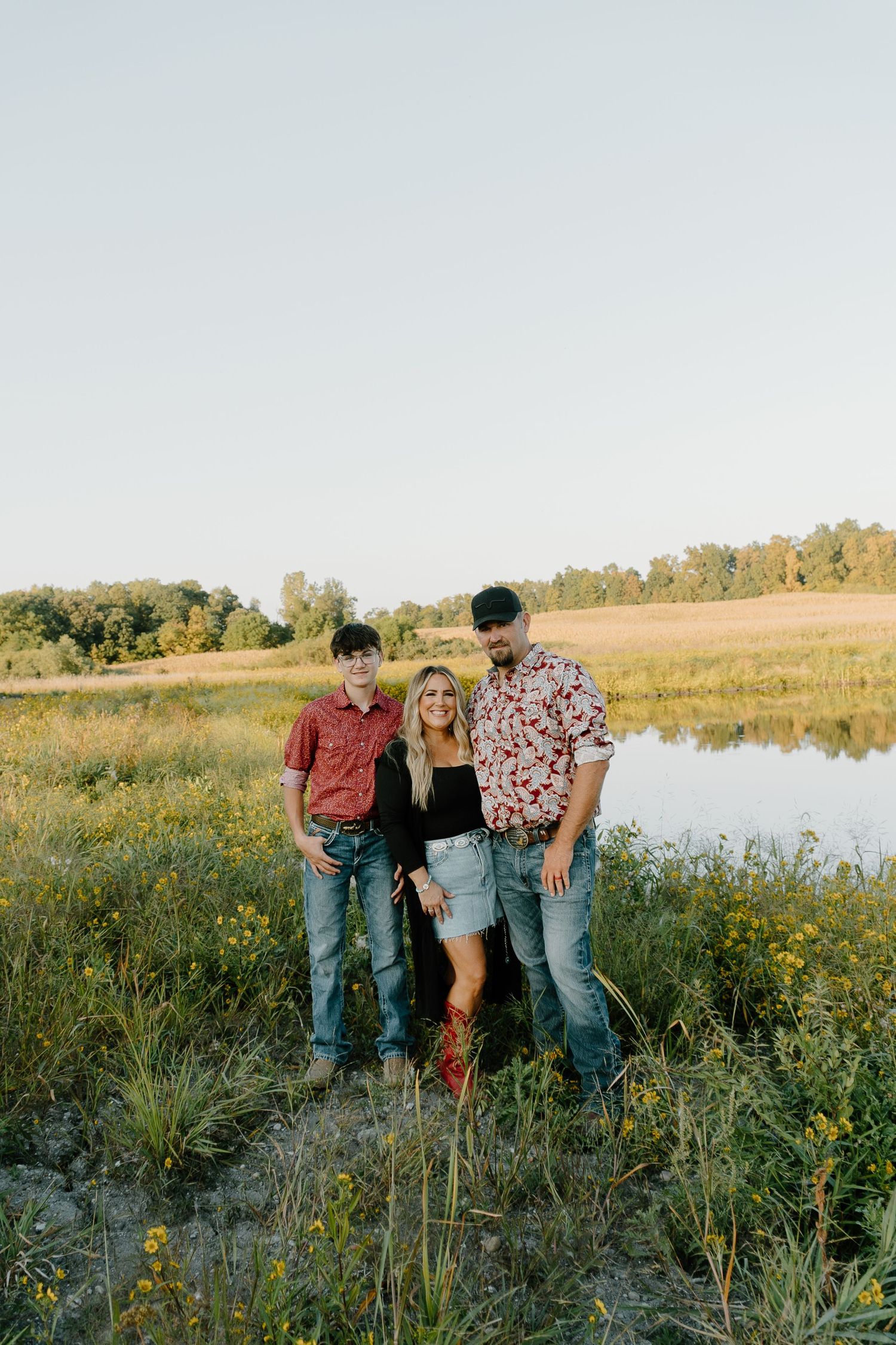 A family stands together in a scenic field with wildflowers and a lake during golden hour.