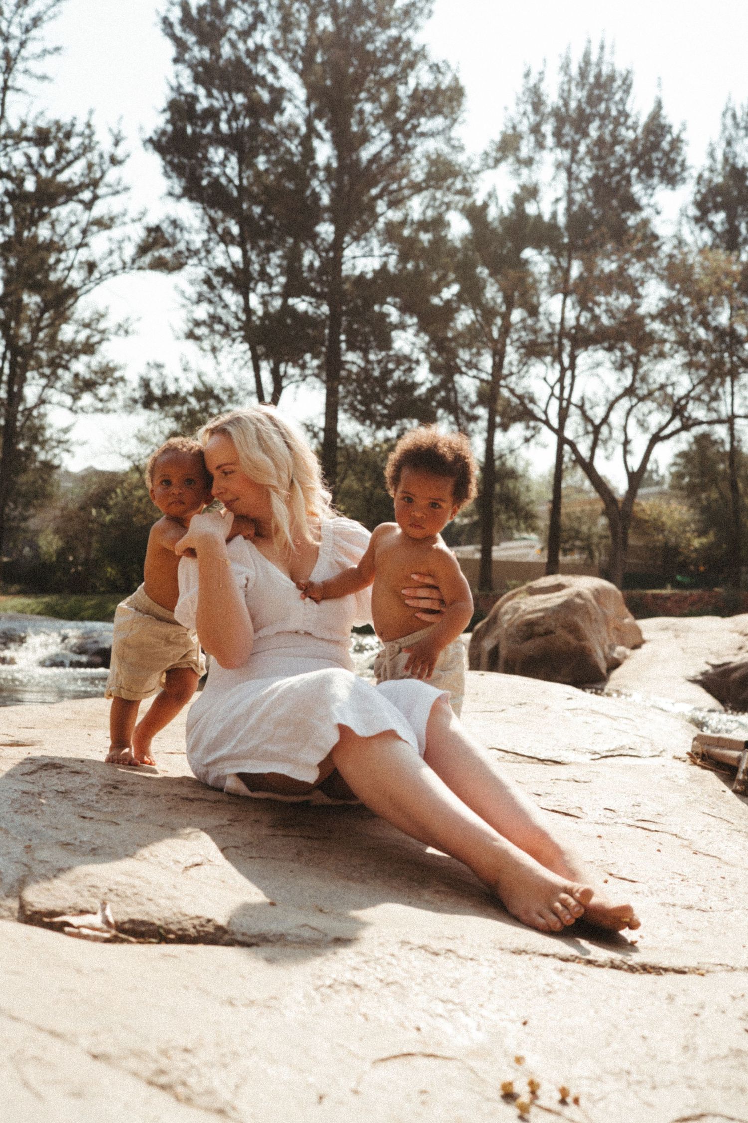 Sun-drenched outdoor photography session on textured rock surfaces, with a mother and her twin babies in Johannesburg