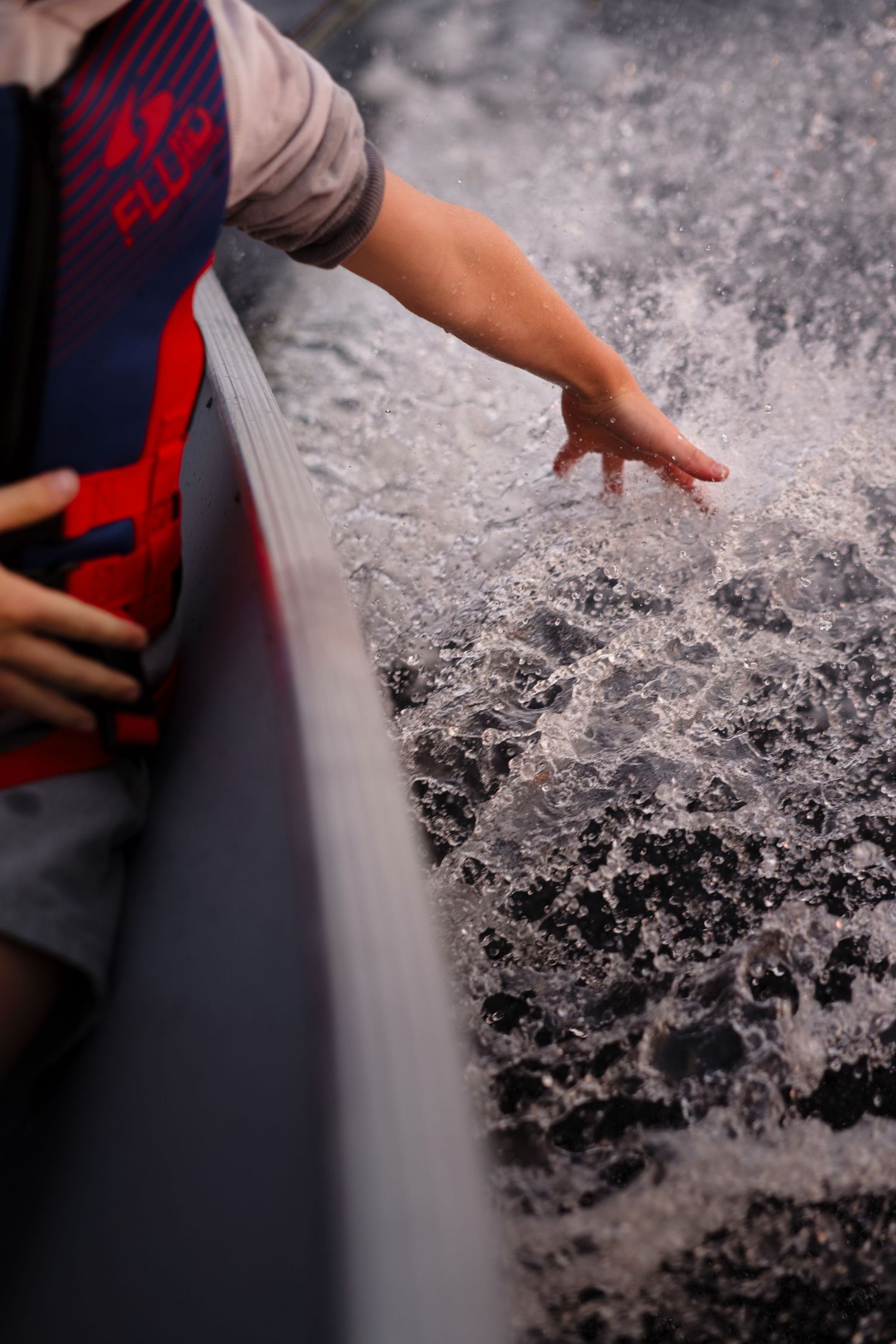 A hand reaches out to touch the churning wake of a boat on the water.