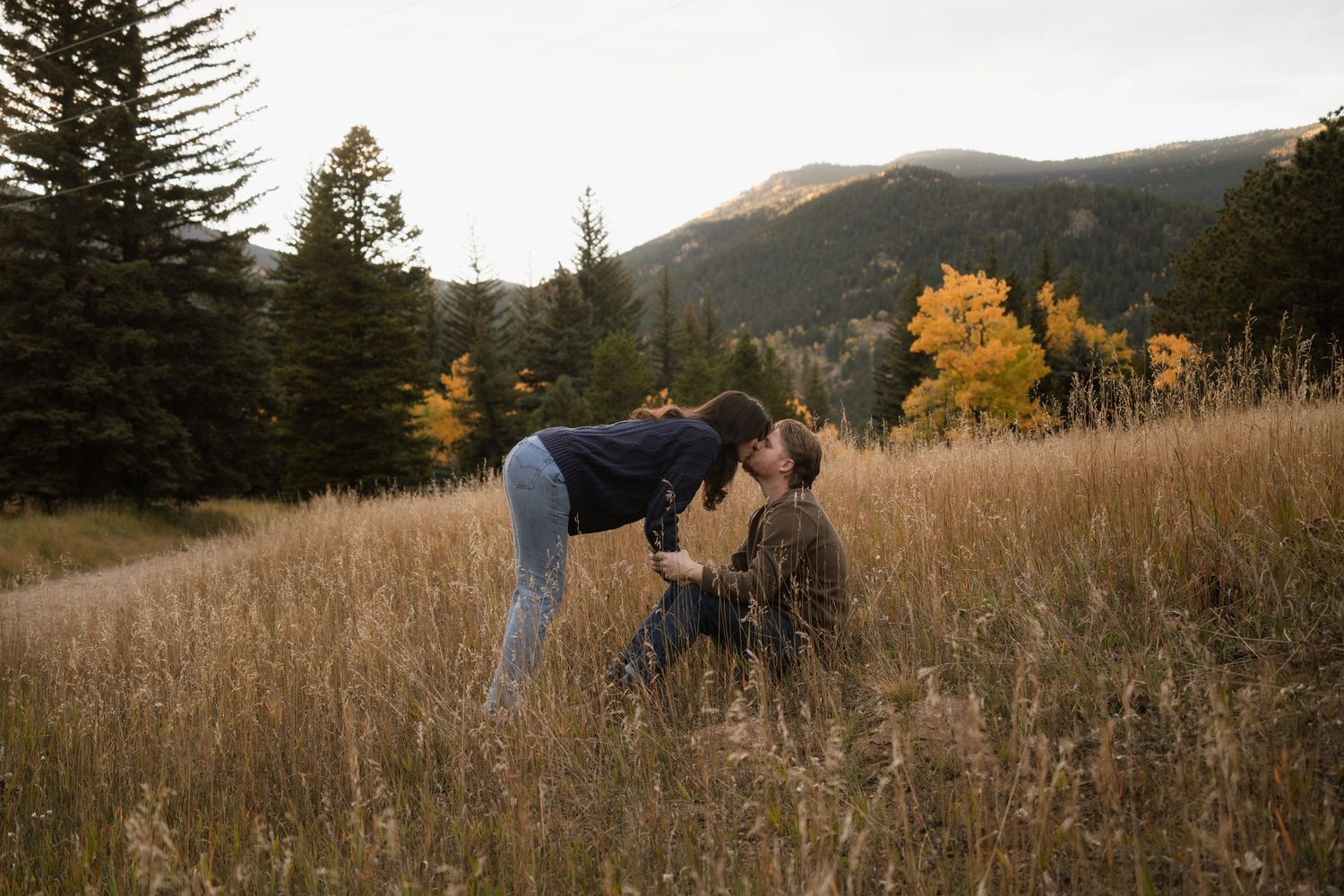 Romantic couple lying in tall grass field wearing white and earth-toned clothing.