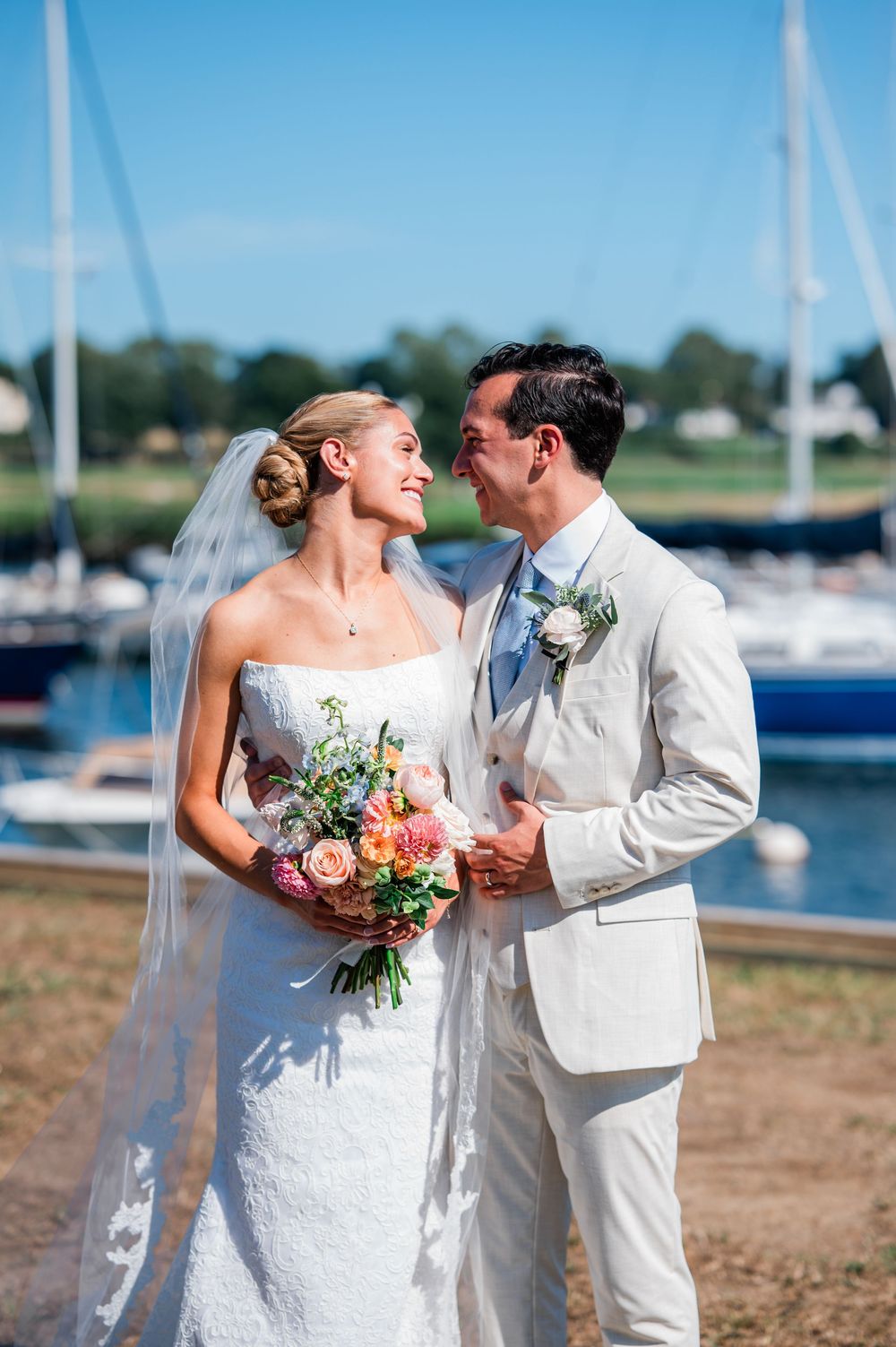 A romantic wedding couple shares intimate moments by a marina with sailboats in the background.
