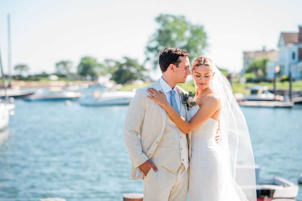 A couple shares a romantic moment on a sunny day by the waterfront with boats in the marina.