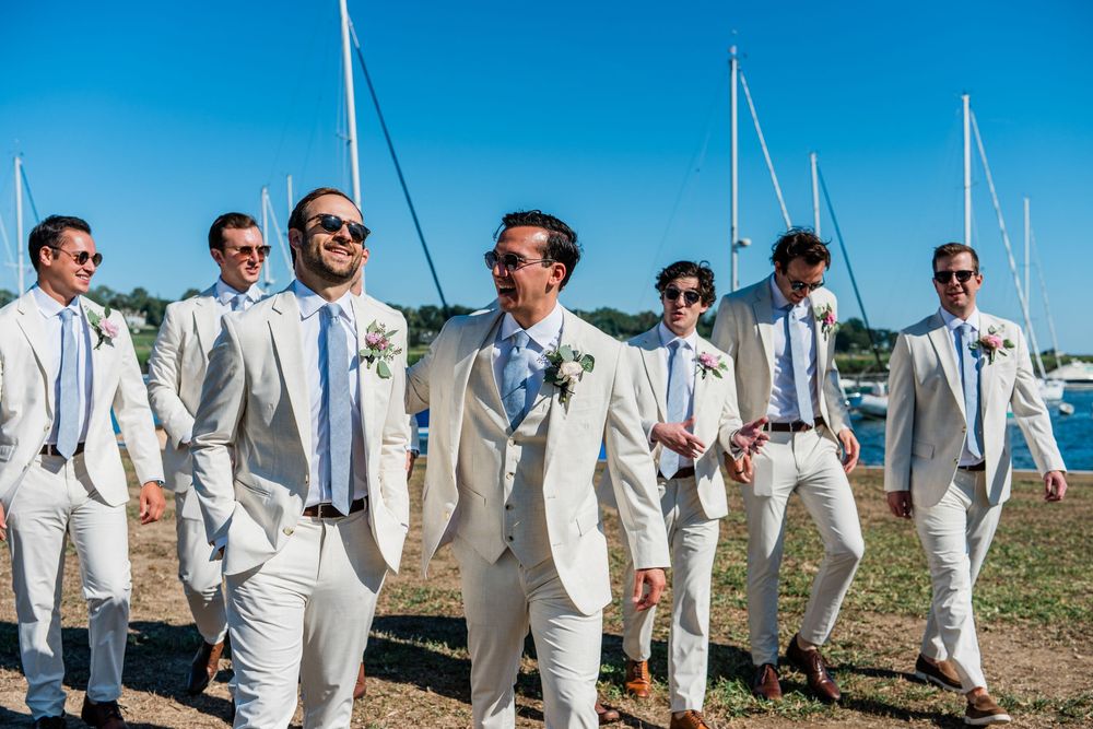 Groomsmen lined up wearing matching light colored suits at a waterfront wedding venue.