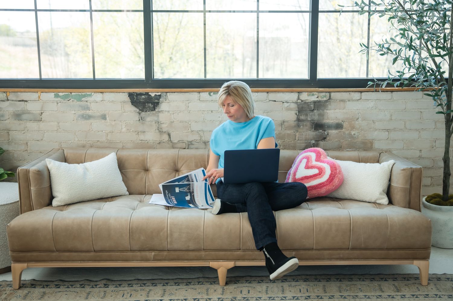 A person lounges comfortably on a modern tan leather sofa while working on a laptop computer.