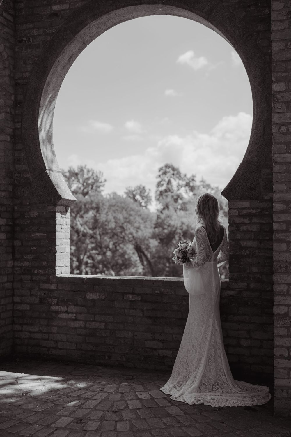 Black and white series showing a bride posing in an arched brick window frame.