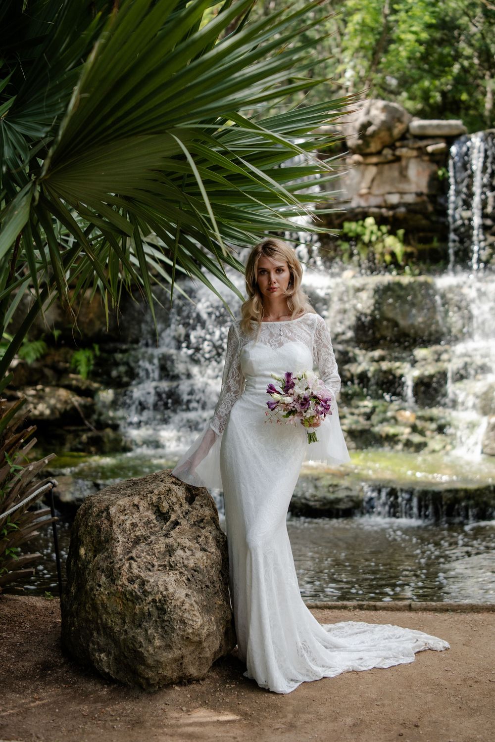 Beautiful bridal portrait by a cascading waterfall with tropical palm leaves and natural scenery.