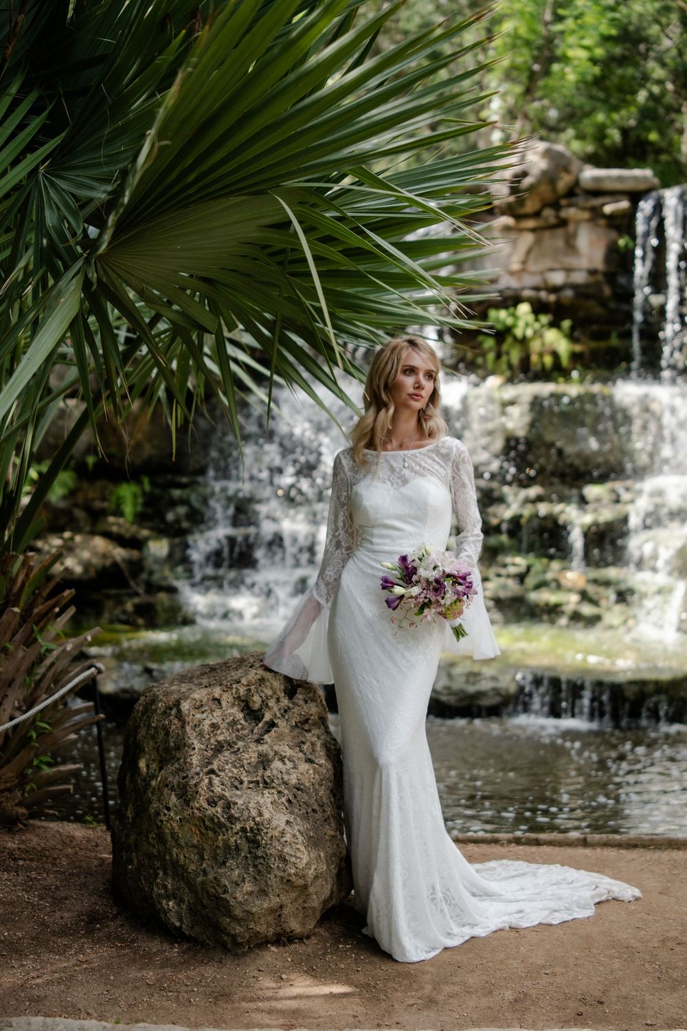 Romantic bridal photos captured near a serene waterfall with lush tropical landscaping.