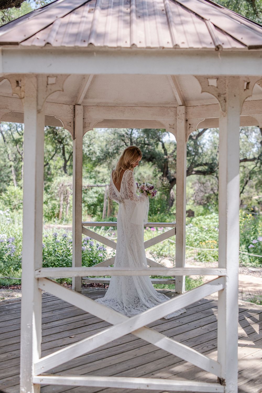 White wooden gazebo in a garden setting provides perfect backdrop for bridal portraits.