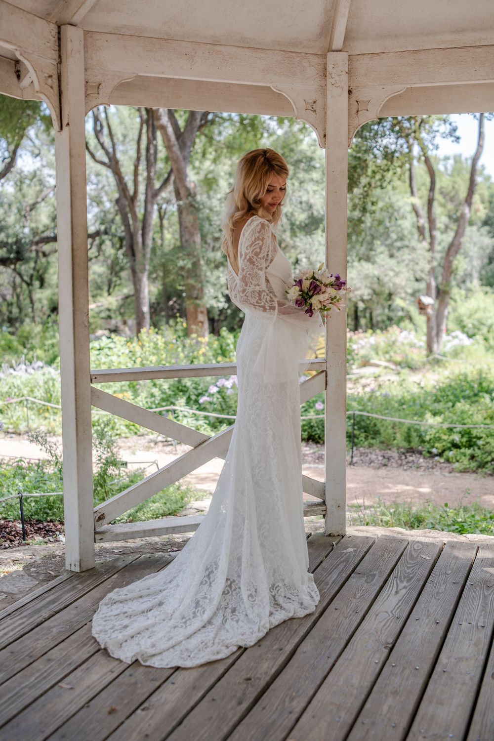 Classic bridal poses on rustic wooden deck of a white gazebo surrounded by greenery.