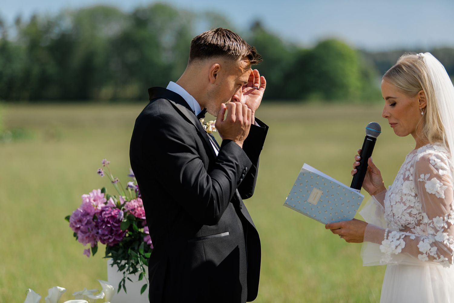 Wedding guests sitting outdoors in sunlight watching ceremony with some wearing sunglasses and formal attire.