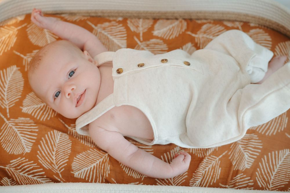 Baby wearing white outfit lies on orange and white patterned blanket in series of connected photos.