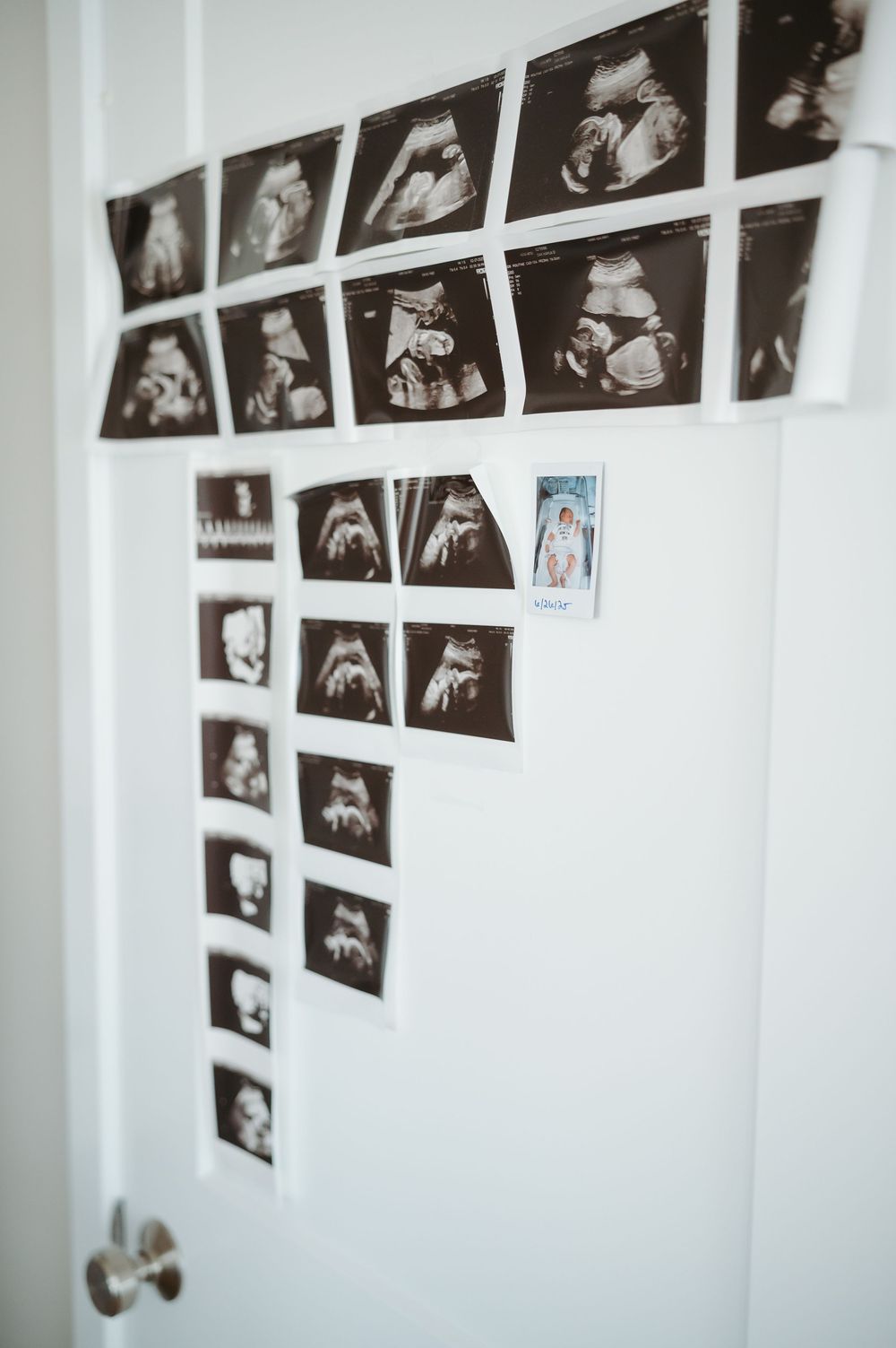 A collection of black and white photographs arranged in rows on a white wall next to a door handle.