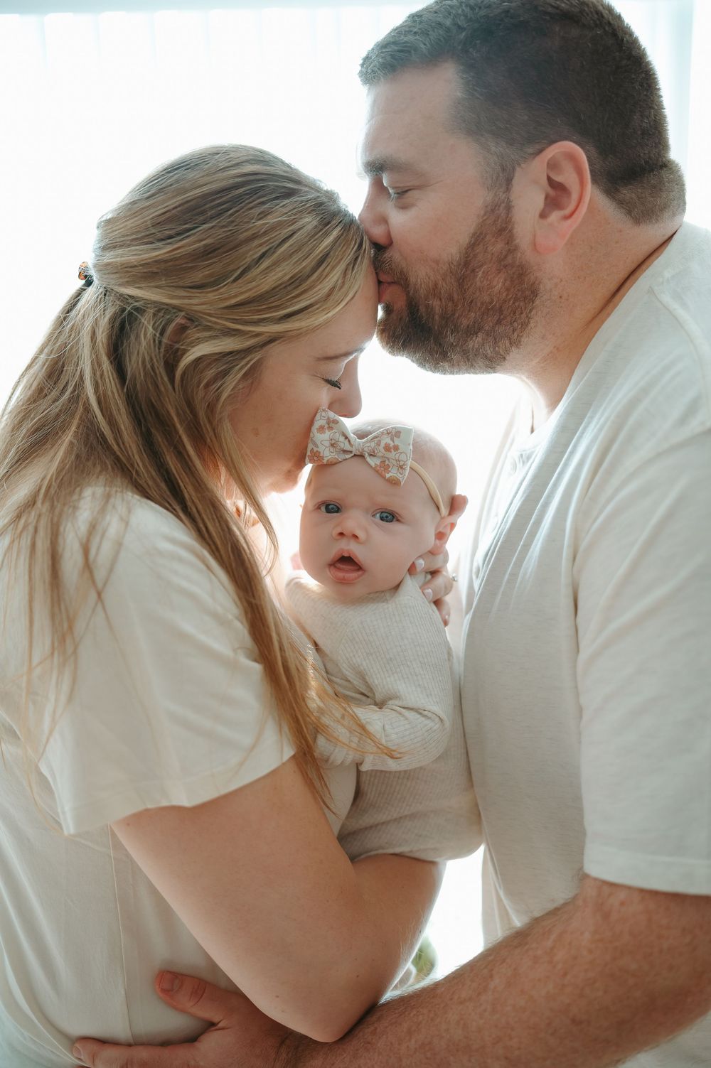 A family in white clothing shares tender moments together in a series of intimate portraits.