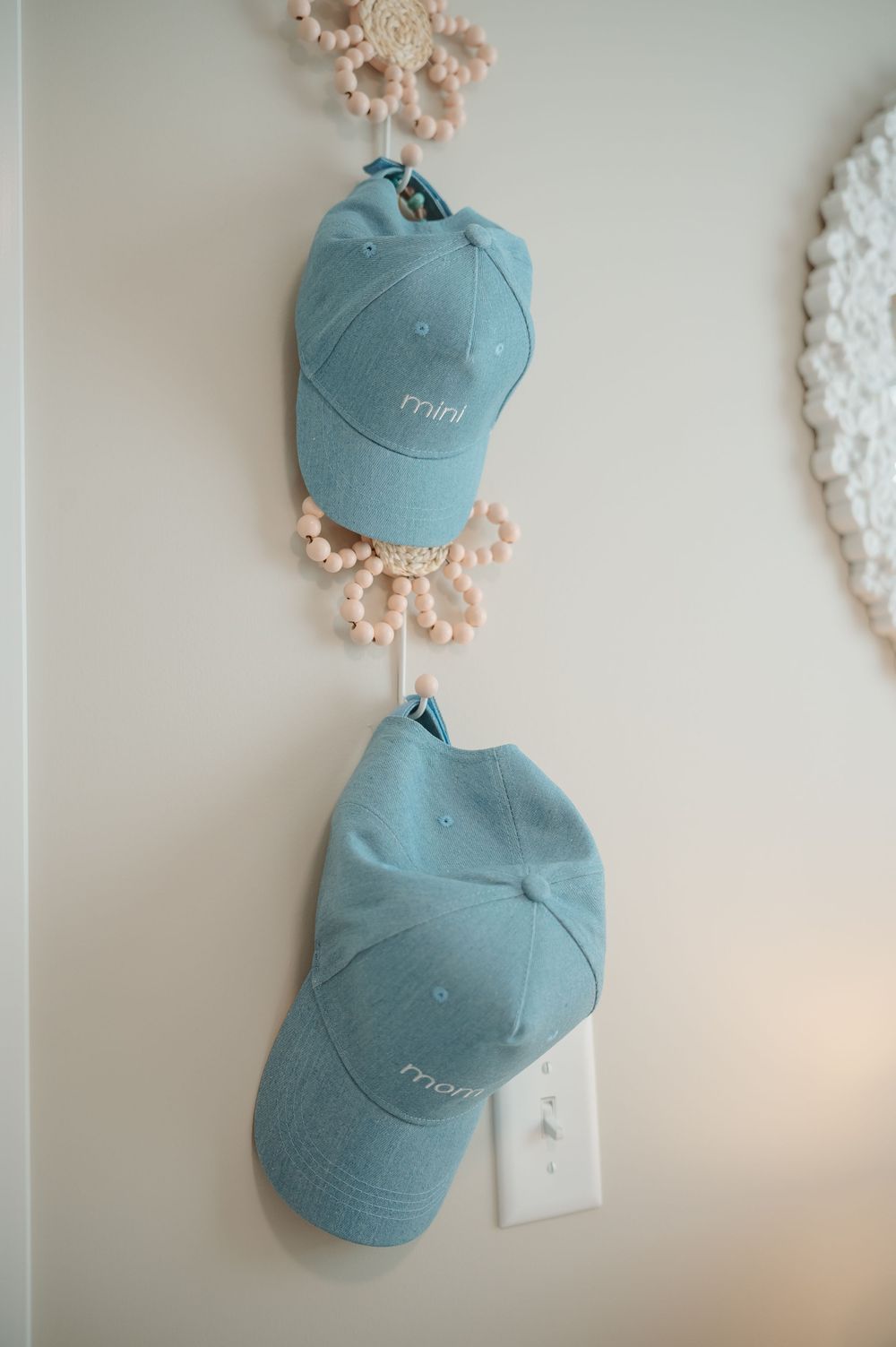 Two light blue baseball caps mounted on a beige wall next to decorative pink and white floral wall decor.